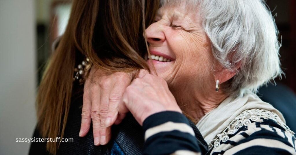 a very happy elderly lady hugs a younger female visitor in her home.