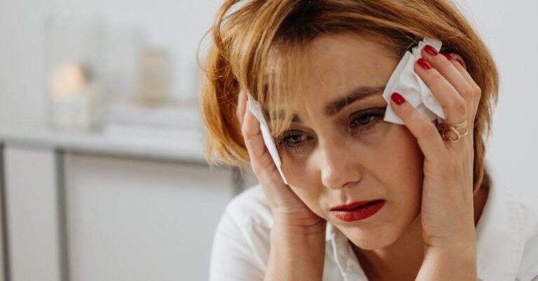 a sad woman with her hands up to her temples dealing with signs of a midlife crisis in women.