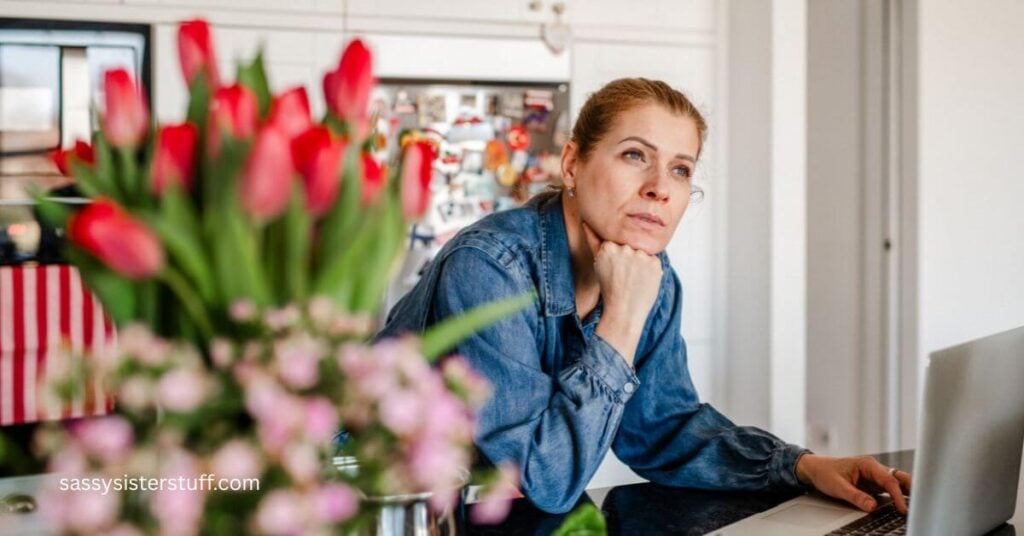 a woman sits at her laptop and stares off into the distance pondering signs of a midlife crisis in women.