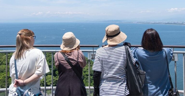 four women traveling after 50 stand together looking out over a large blue body of water.