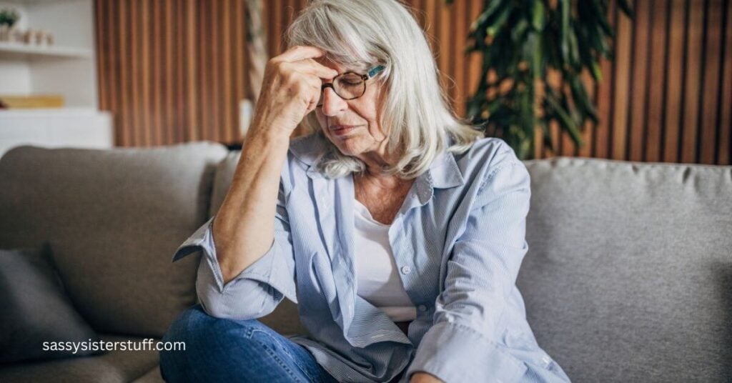gray haird middled aged woman sits with her hand up to her head pondering the signs of a midlife crisis in women.